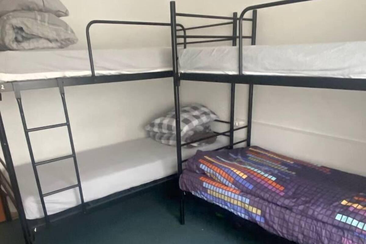 A bunk bed room with a ladder on the left side and a colorful blanket on the lower bunk.