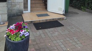 Ein Gebäudeeingang mit einer Steinfassade, einer Treppe, die zum Eingang führt, und einem Blumenkasten davor.