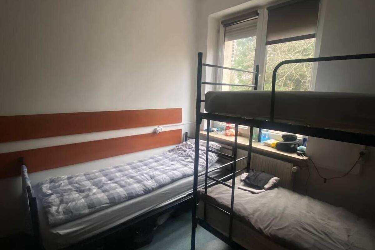A dormitory room with bunk beds, a window, and a radiator.