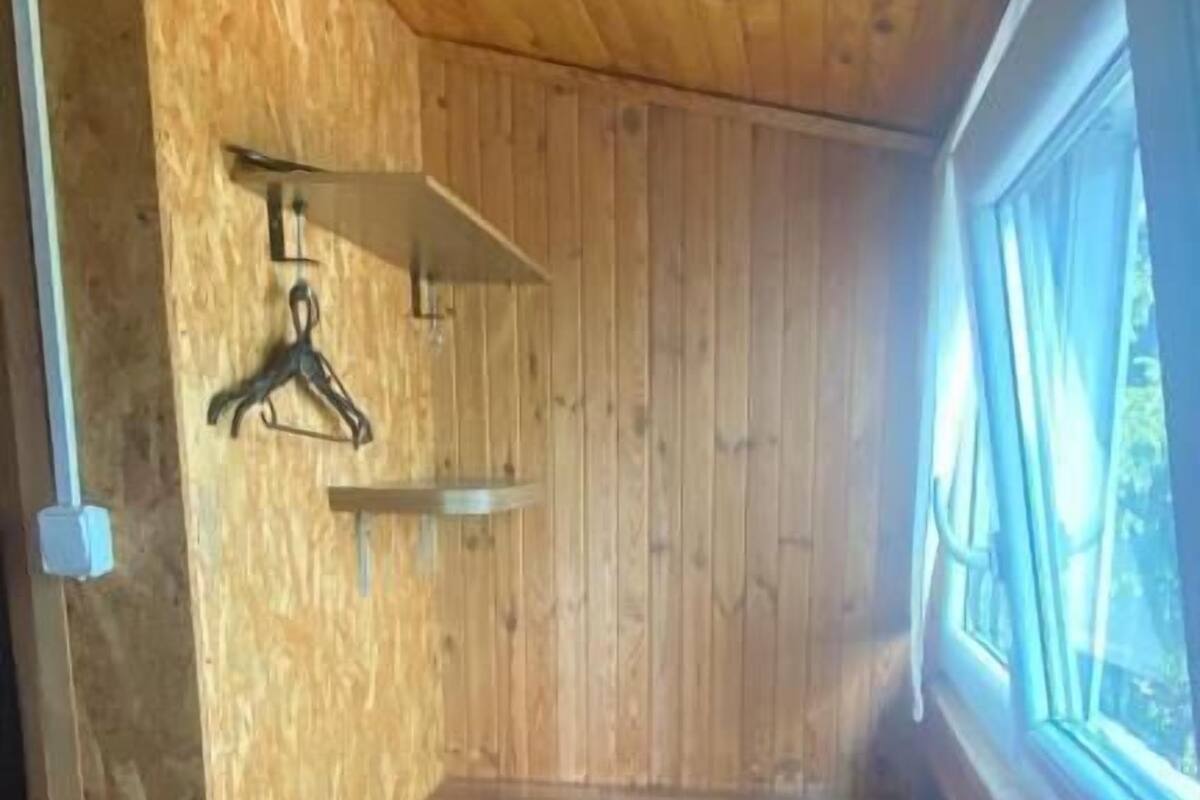 A small, enclosed room with a wooden ceiling and walls, a single chair, a small table, and a window with curtains.