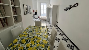 Un pasillo estrecho con una mesa de comedor preparada para dos personas, una estantería y una puerta que da a otra habitación.