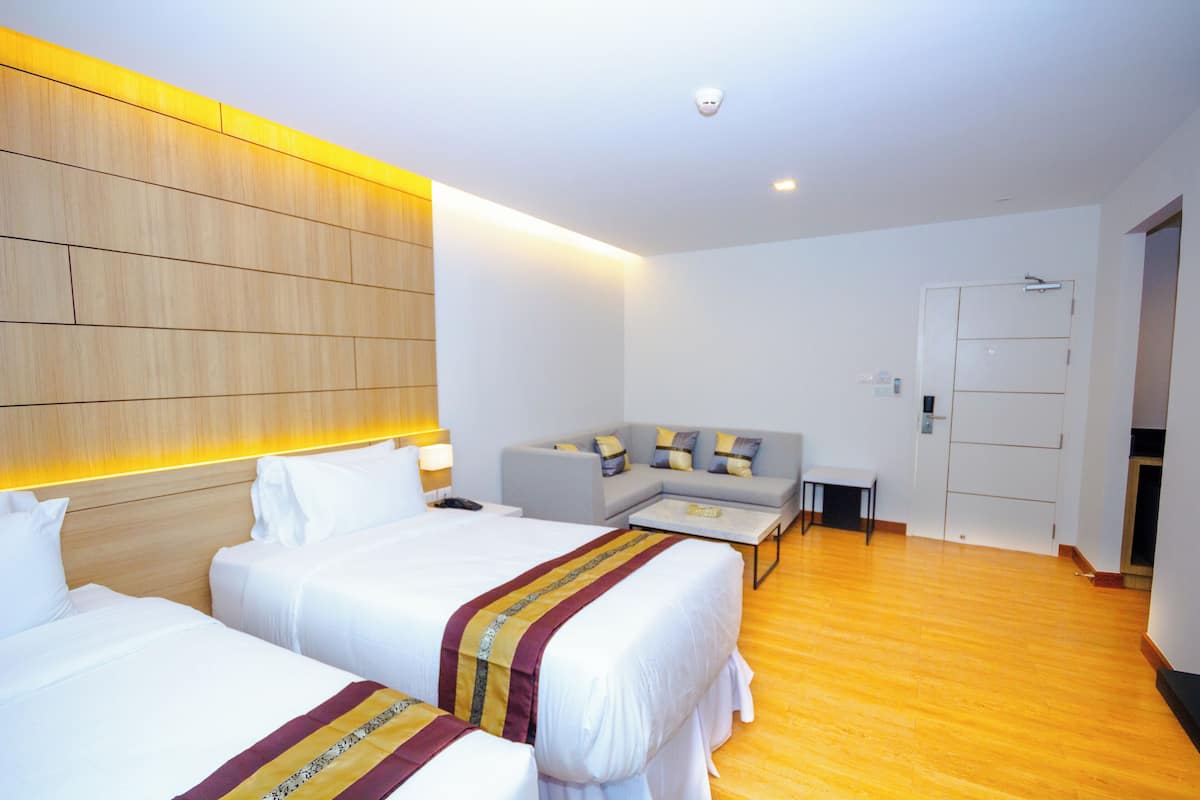 A hotel room with two beds, a sofa, a small table, and a wooden headboard.