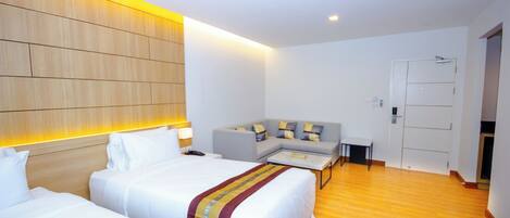 A hotel room with two beds, a sofa, a small table, and a wooden headboard.