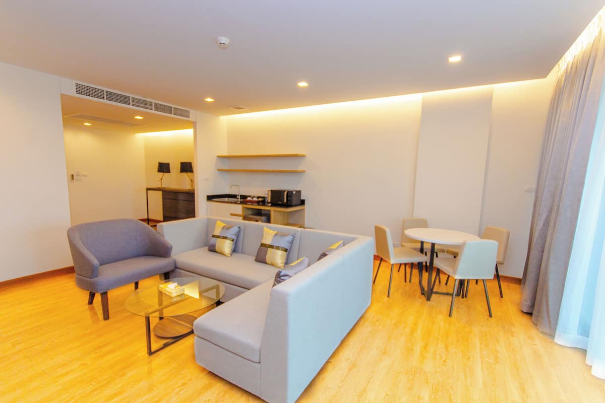 A modern living room with a grey sofa, a glass coffee table, and a dining area with a white table and chairs.