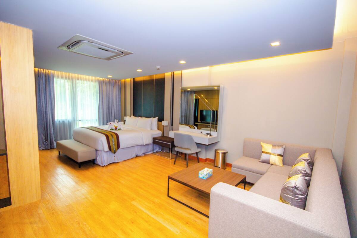 A hotel room with a bed, a sofa, a coffee table, a desk, and a mirror.