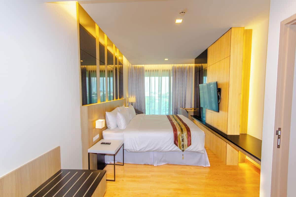 A modern hotel room with a large bed, a bedside table, a TV, and a wooden floor.