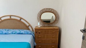 A bedroom with a bed, a wooden dresser, and a mirror.