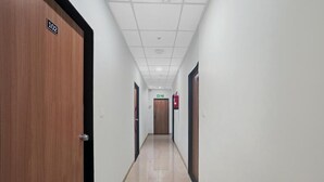 A hallway with a wooden door labeled "102" on the left, a fire extinguisher mounted on the wall, and a door at the end of the hallway. - HOTEL WOW (Surat)