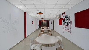 A modern dining area with white tables and chairs, a ceiling fan, and motivational wall art. - HOTEL WOW (Surat)