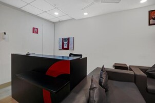 Un área de recepción con un escritorio negro, detalles rojos, una pizarra de anuncios y un sofá de cuero marrón.