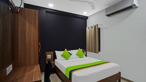 A hotel room with a bed, a wooden wardrobe, a desk, a ceiling fan, and an air conditioning unit. - HOTEL WOW (Surat)
