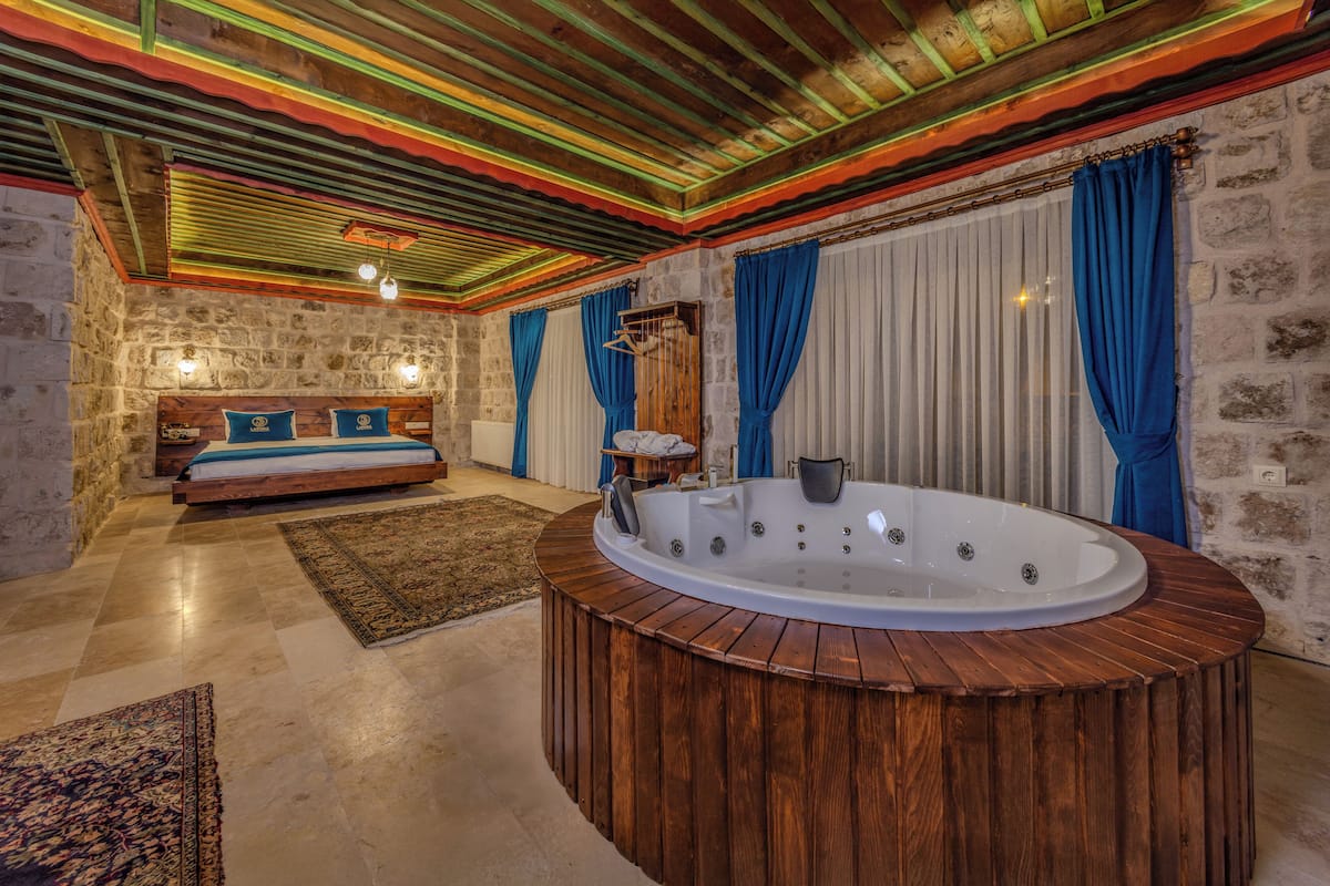Una habitación con una bañera de madera, una cama con almohadas azules y una pared de piedra.