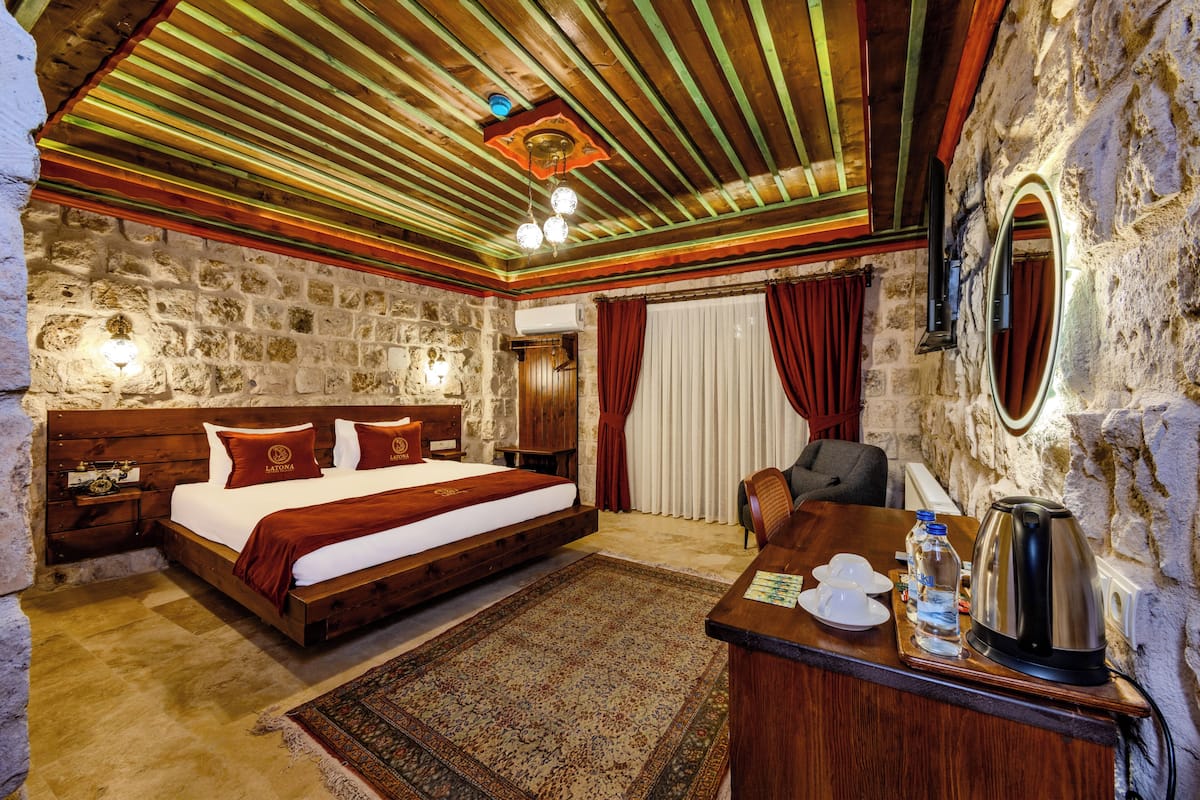 Un dormitorio con una cama de madera, un escritorio con un hervidor y una pared de piedra.