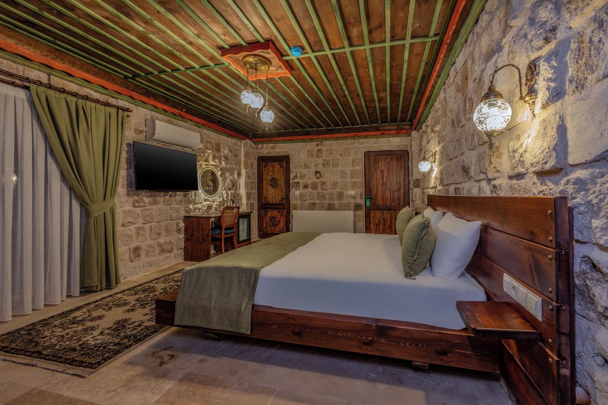 Un dormitorio con cama de madera, paredes de piedra, televisor de pantalla plana y chimenea de piedra.