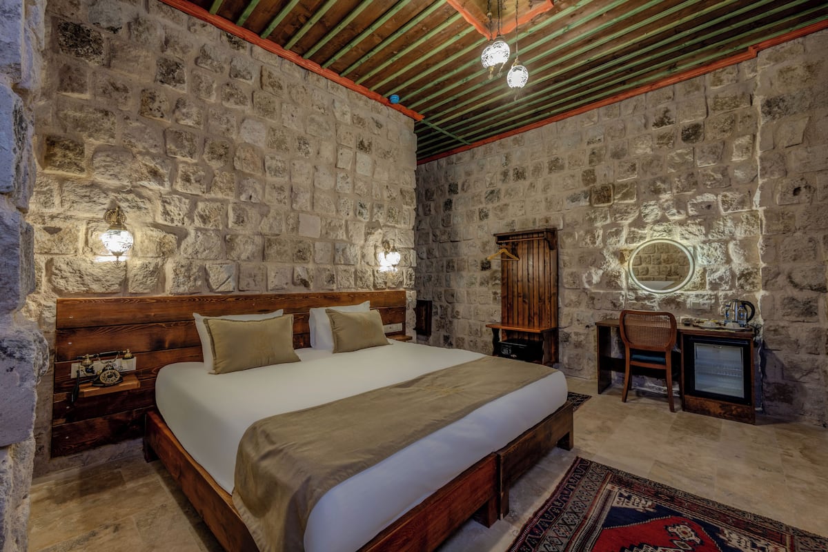 Un dormitorio con paredes de piedra, una cama de madera, mesitas de noche, un escritorio y un espejo.