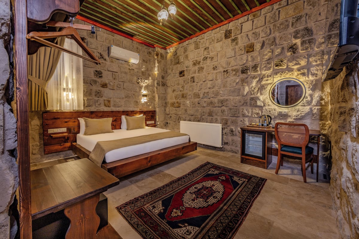 Un dormitorio rústico con una cama de madera, un escritorio pequeño, una silla y una alfombra decorativa.