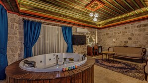 Une pièce avec une baignoire en bois, un canapé, une télévision et un mur en pierre.