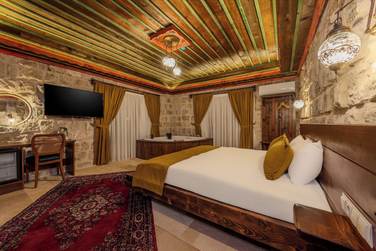 Un dormitorio con una cama de madera, televisor, escritorio y pared de piedra.