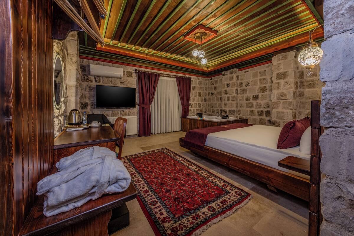 Una habitación con una cama de madera, un escritorio con una silla, una televisión y una pared de piedra.
