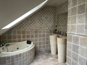 Une salle de bain avec une baignoire sur pieds, deux vasques et un plafond en pente doté d’un puits de lumière.