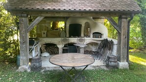 Eine rustikale Außenküche mit einem Steinkamin, einem runden Holztisch und einem Metallstuhl.