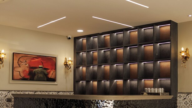 A modern restaurant interior with a marble countertop, seating area, and a wall-mounted light fixture. - Hotel Skyvista (Indore)