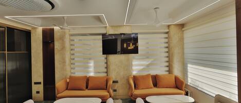 A modern lounge area with two sofas, a flat-screen TV, and a ceiling fan.