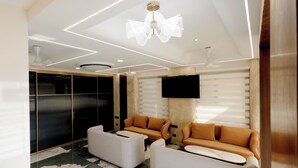 A modern living room with a large flat-screen TV, two sofas, a coffee table, and a decorative ceiling light. - Hotel Skyvista (Indore)