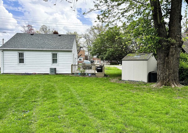 A white single-story house with a fenced yard, a small shed, and a large tree.