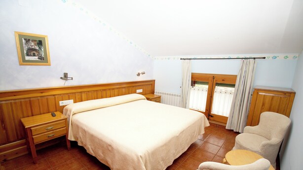 A bedroom with a bed, a nightstand, a chair, a small table, a window with curtains, and a picture on the wall. - Hotel La Botiga (Prades)