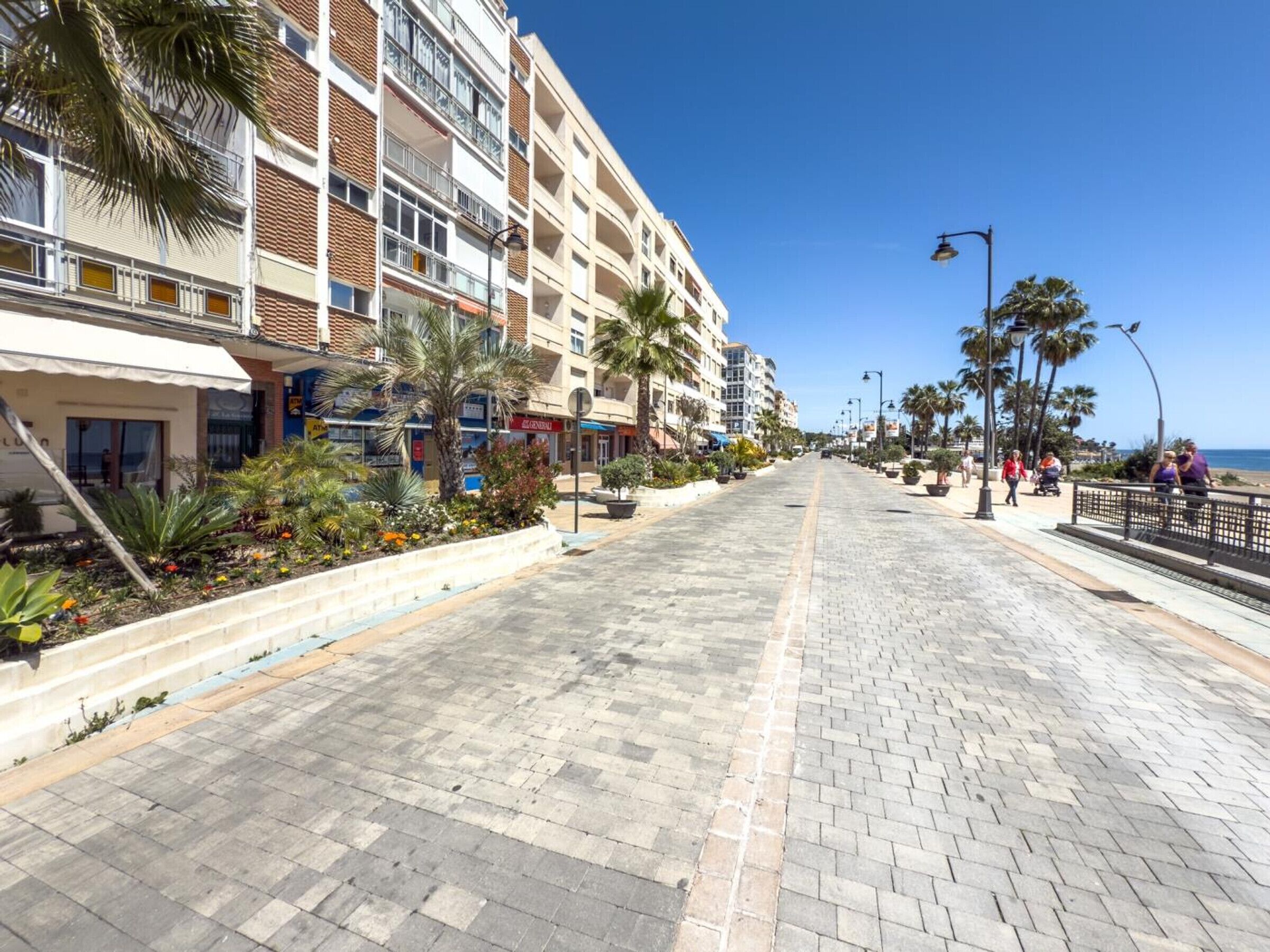 Une promenade dallée, bordée de bâtiments d’un côté et offrant une vue dégagée sur la mer de l’autre.