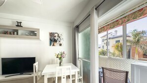A modern living room with a flat-screen TV, a dining table with chairs, a vase with flowers, and a balcony with a chair. - Central Apartment with Balcony in Estepona (Estepona)