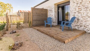 A patio with two blue chairs, a wooden deck, and a stone wall. - Jungle Studio with Terrace and Heated Pool near Nantes (Port-Saint-Père)