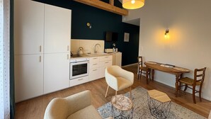 A compact kitchen with white cabinets, a wooden ceiling, and a dining area with a table and chairs. - Jungle Studio with Terrace and Heated Pool near Nantes (Port-Saint-Père)
