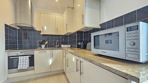 Een moderne keuken met witte kasten, een ingebouwde oven, een magnetron en een zwart betegelde spatwand.