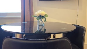 Een ronde tafel met een vaas witte bloemen, zwarte stoelen en een flatscreen televisie aan de muur.