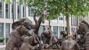 Een bronzen beeldhouwwerk van verschillende dieren verzameld rond een tafel, waarschijnlijk een tafereel uit een verhaal of mythe.