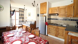 A compact kitchen with wooden cabinets, a refrigerator, and a dining area with a table set for four. - Aussois apartment for 6 with balcony and internet access (Aussois)