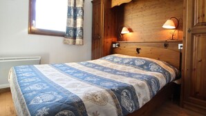 A bedroom with a wooden headboard, a quilted bedspread, two bedside lamps, and a window with a curtain. - Aussois apartment for 6 with balcony and internet access (Aussois)