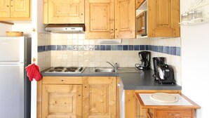 A compact kitchen with wooden cabinets, a built-in stove, a sink, and a coffee maker. - Aussois apartment for 6 with balcony and internet access (Aussois)