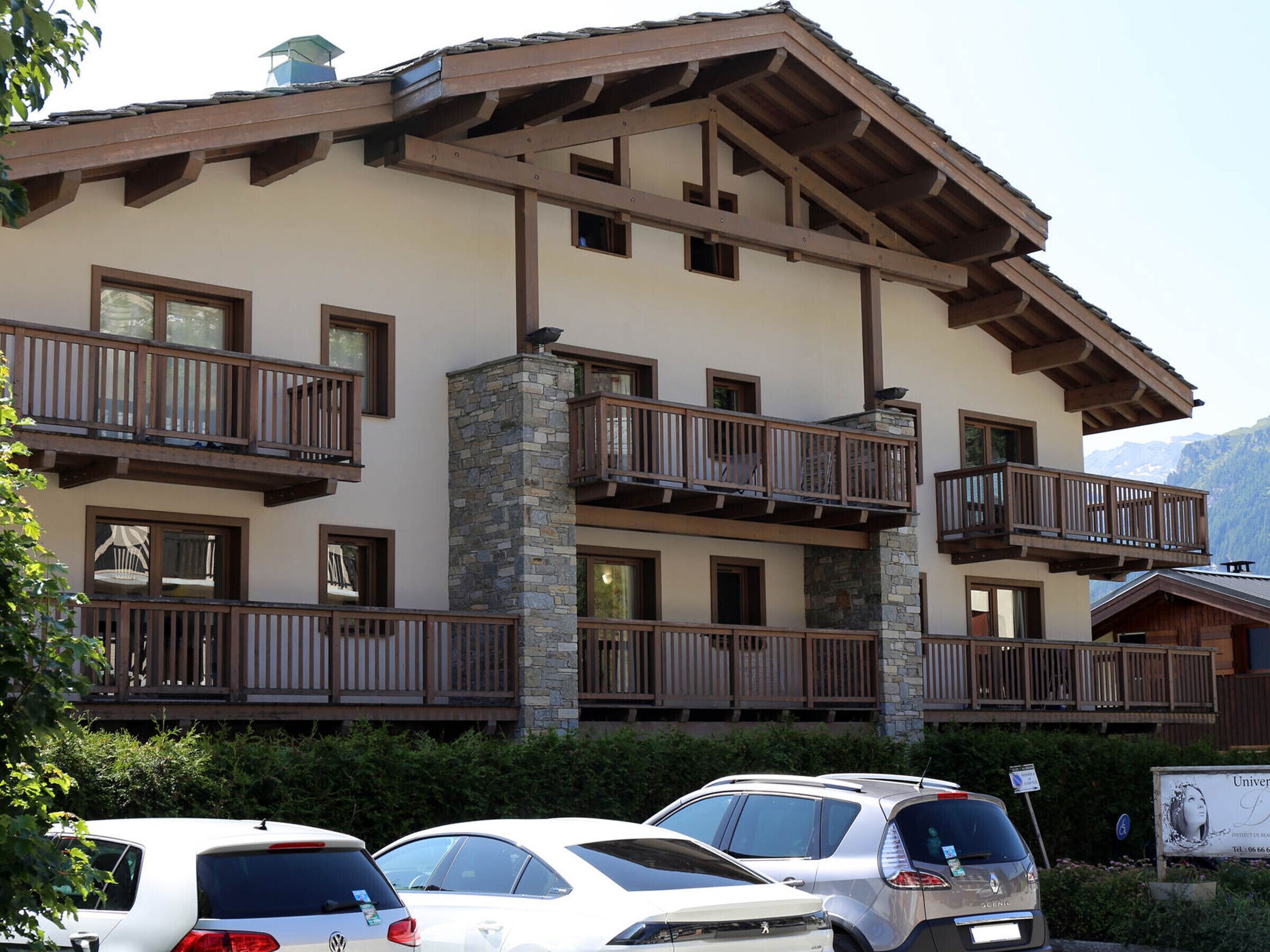 A multi-story hotel with balconies, a stone facade, and a parking area with cars.