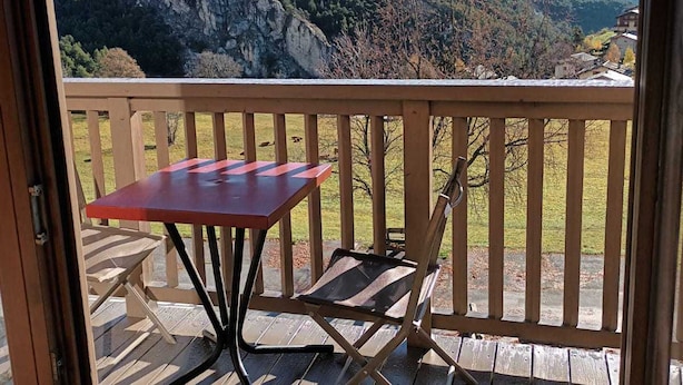 A balcony with a table and two chairs, overlooking a mountainous landscape with snow-capped peaks.
