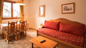 A cozy living room with a wooden sofa, a dining table with chairs, and a small table with a remote control. - Cozy apartment with parking, sleeps 4, near shuttles in Aussois (Aussois)