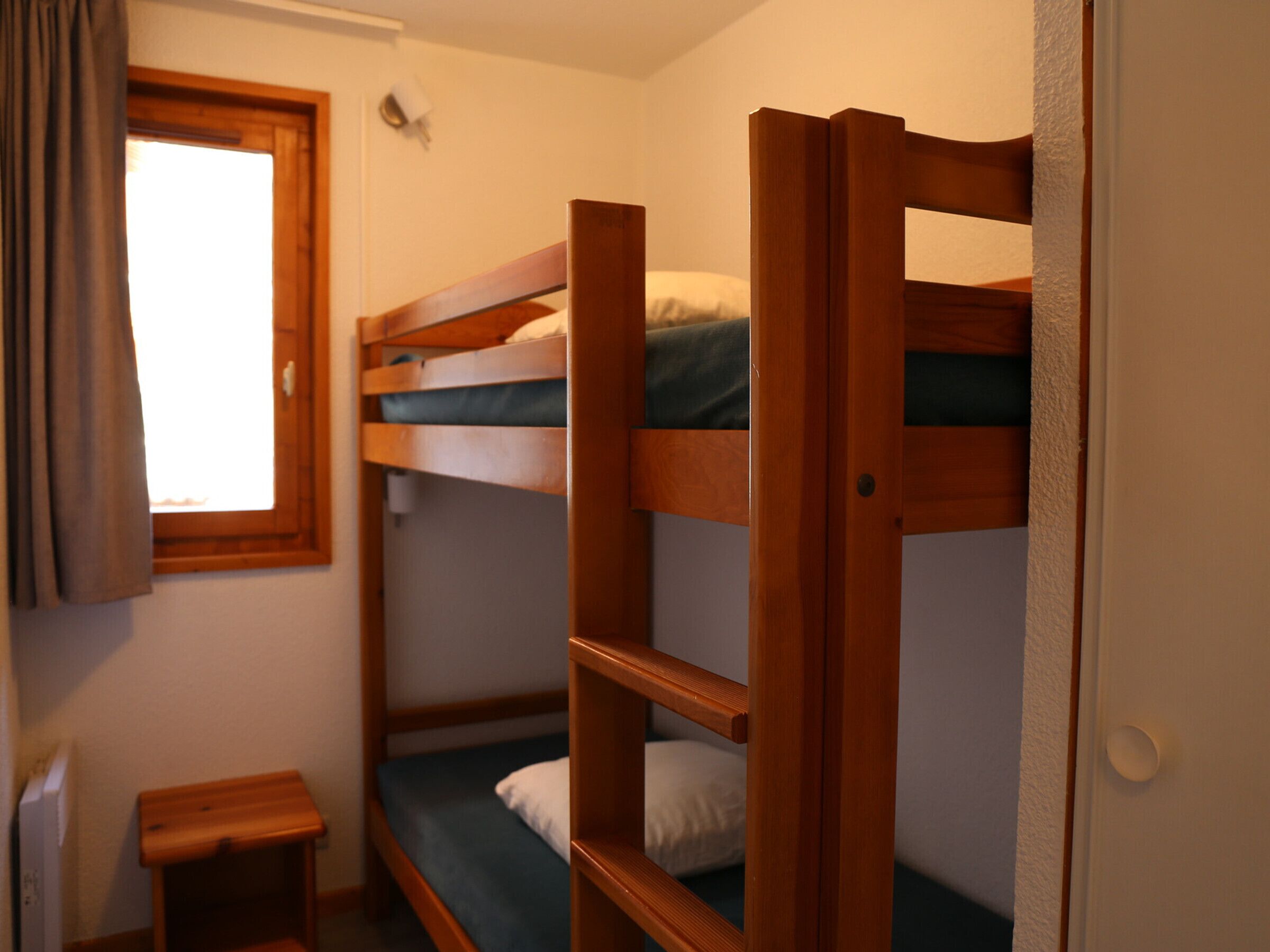Dormitorio con literas, una mesita de madera pequeña y una ventana con cortinas.