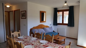 A cozy room with a bed, a dining table set for four, and a window with curtains. - Comfortable apartment in Aussois for 6 with terrace (Aussois)