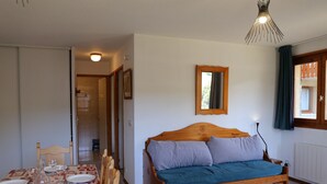A room with a wooden bed, a dining table set for four, and a small wooden table. - Comfortable apartment in Aussois for 6 with terrace (Aussois)