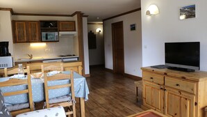 A compact living space with a kitchenette, a dining area with a table and chairs, a TV on a wooden cabinet, and a hallway leading to another room.