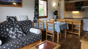 A cozy living room with a sofa and a dining table, a kitchen with wooden cabinets, a microwave, and a coffee maker.