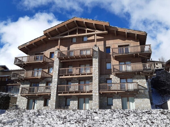 A multi-story hotel with balconies, stone facade, and a ski slope in the background.