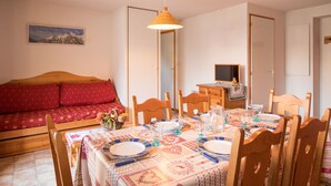 Una habitación acogedora con un sofá de madera, una mesa de comedor con platos y vasos, y un pequeño televisor sobre un aparador.